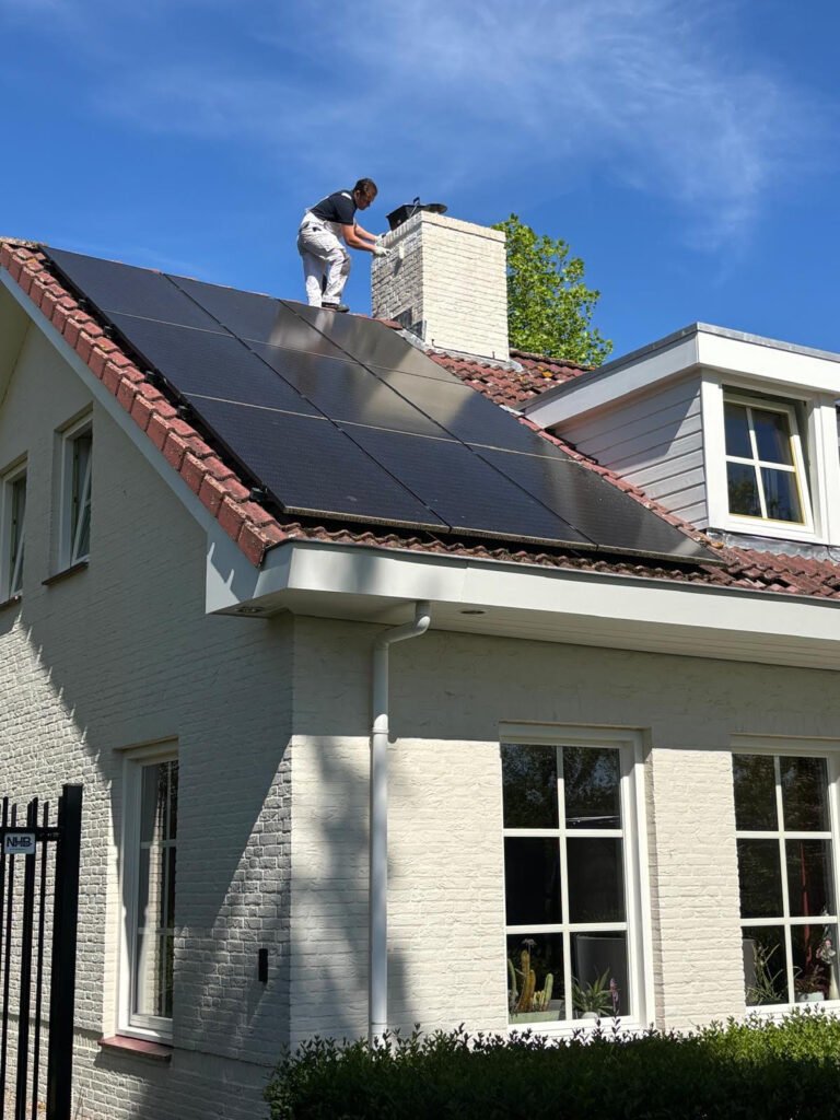 Schilder van Meulendijks Schilderservice aan het werk op het dak met muurverf onder een strakblauwe lucht