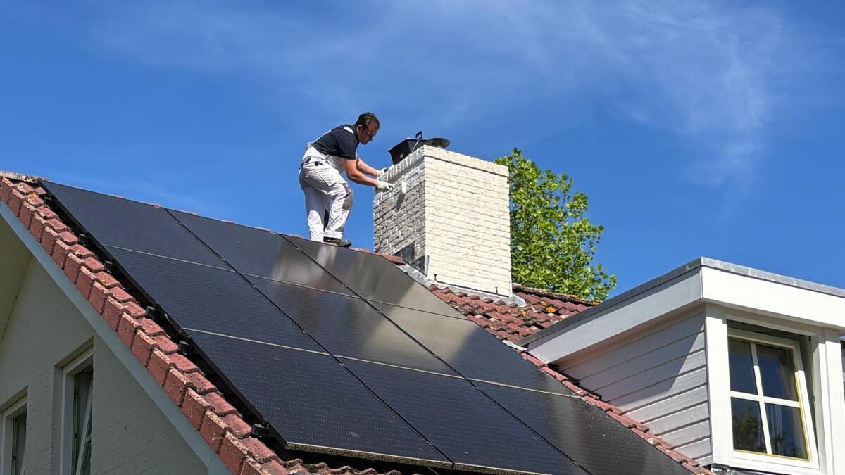 Schilder van Meulendijks Schilderservice aan het werk op het dak met muurverf onder een strakblauwe lucht